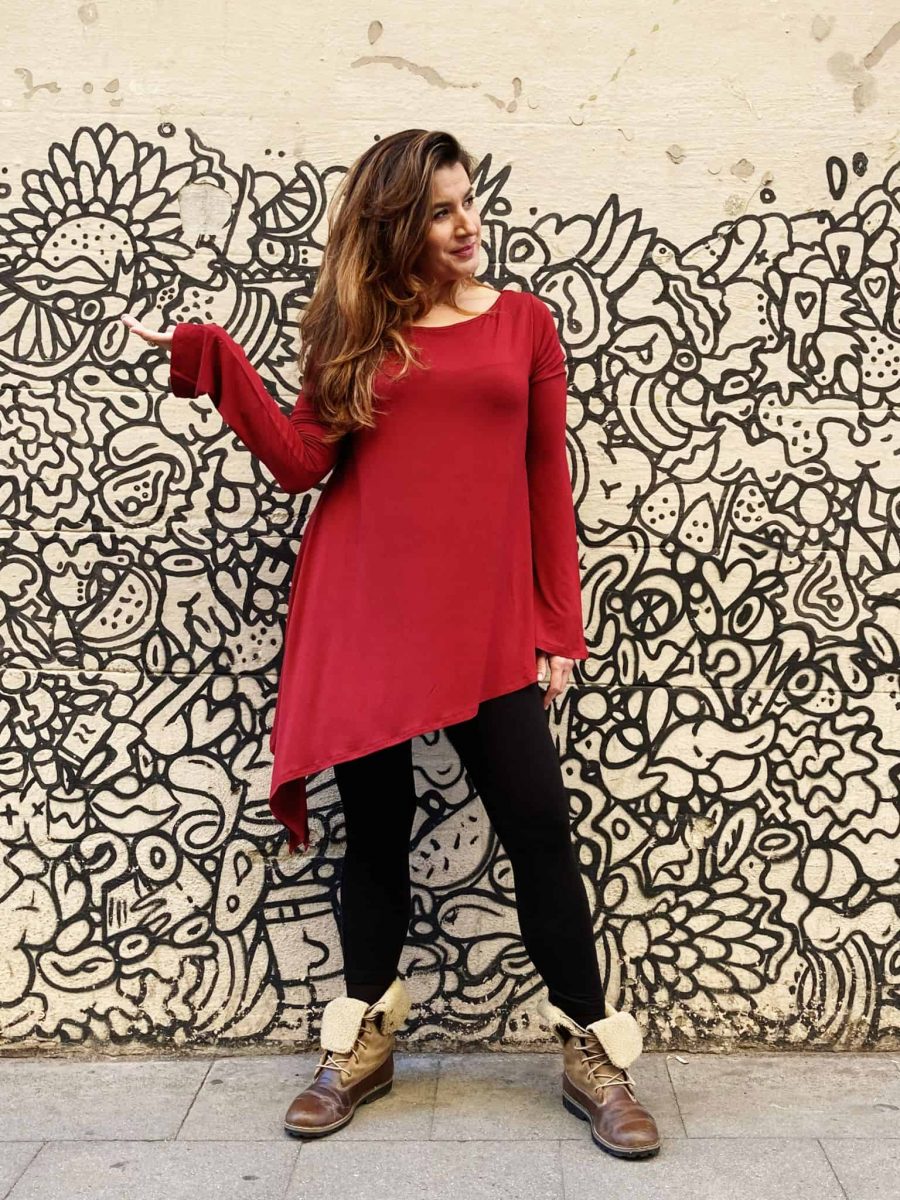 clienta en las calles de Barcelona, cerca a la tienda, luciendo la tunica larga, corte irregular, cuello barco y manga larga en color rojo con leggins negros.