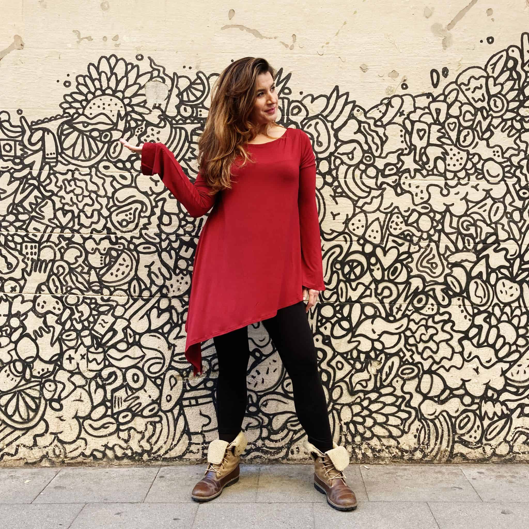 clienta en las calles de Barcelona, cerca a la tienda, luciendo la tunica larga, corte irregular, cuello barco y manga larga en color rojo con leggins negros.