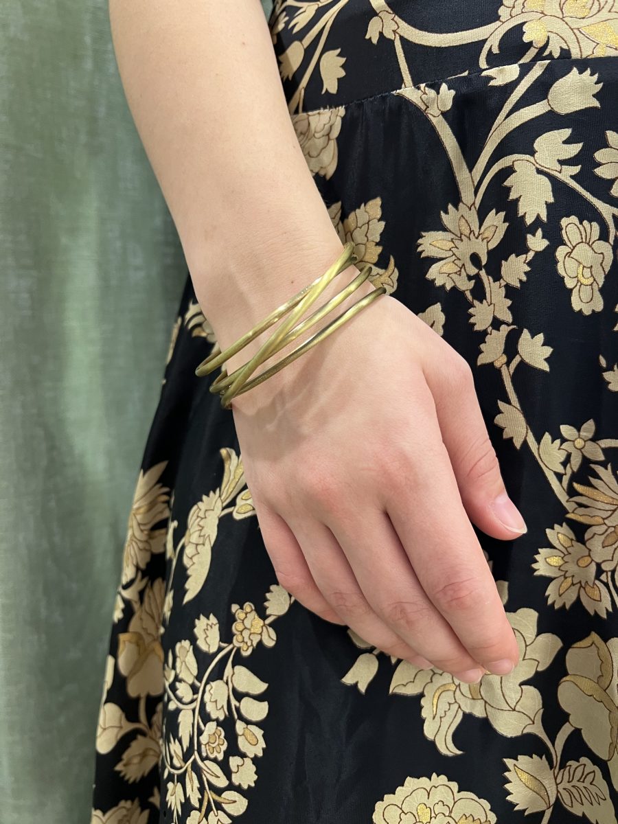 mano de una mujer llevando una pulsera de laton color dorado frente a un fondo negro con flores doradas.
